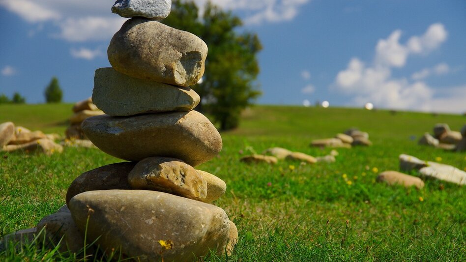 Steinbalance am Kraftweg in Bad Loipersdorf im Thermen- & Vulkanland Steiermark, umgeben von grüner Wiesenlandschaft und weiteren Natursteinen.