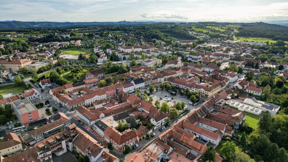 Luftaufnahme der historischen Altstadt von Fürstenfeld im Thermen- & Vulkanland Steiermark mit geschlossenem Häuserensemble, rotdachigen Bürgerhäusern, Hauptplatz und umliegender grüner Hügellandschaft an einem sonnigen Tag.
