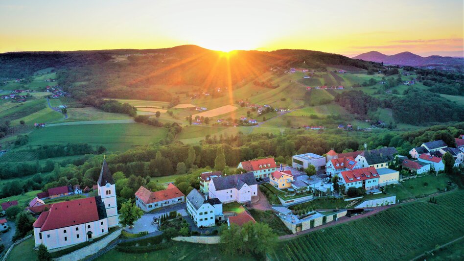 Sonnenuntergang über grünen Hügeln, steilen Weinhängen und der Kirche in St. Anna am Aigen im Thermen- & Vulkanland Steiermark