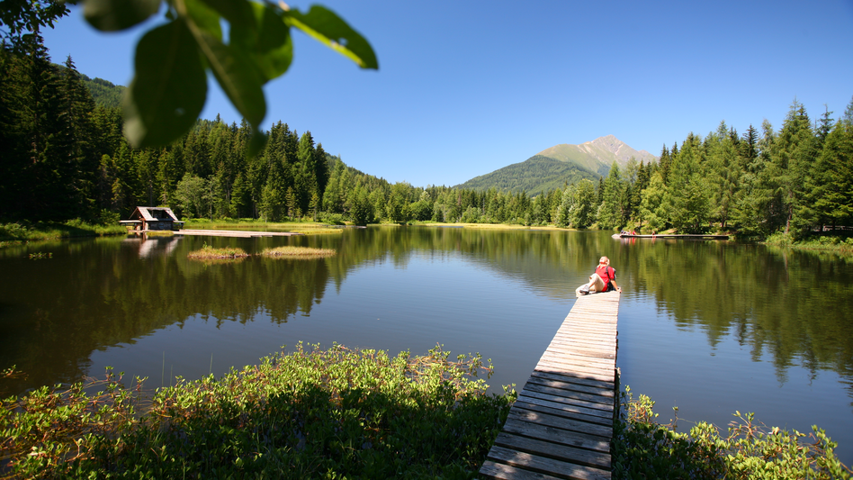 Eine Person relaxt an einem sommerlichen Tag am Steg am See
