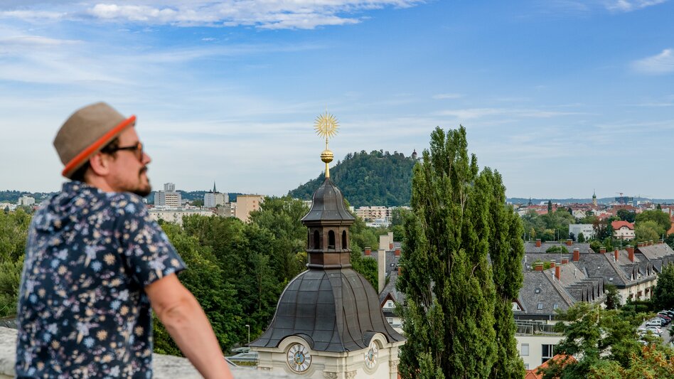 Person genießt den Ausblick vom Grazer Kalvarienberg auf die Stadt und den Schlossberg.