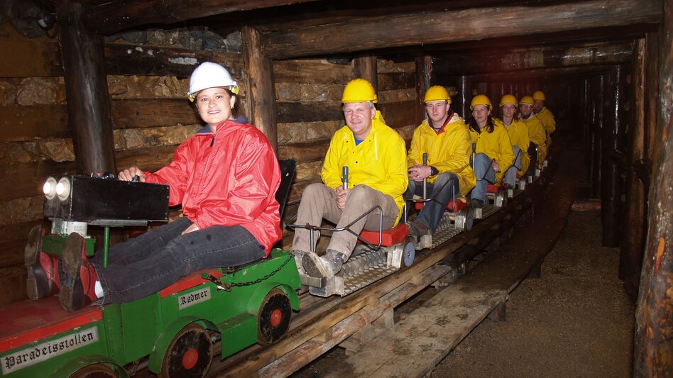 Sieben Menschen sitzen hintereinander auf der Stollenbahn und lächeln in die Kamera