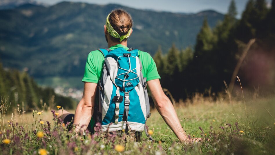 Ein Wanderer sitzt auf einer Wiese und blickt in die Ferne