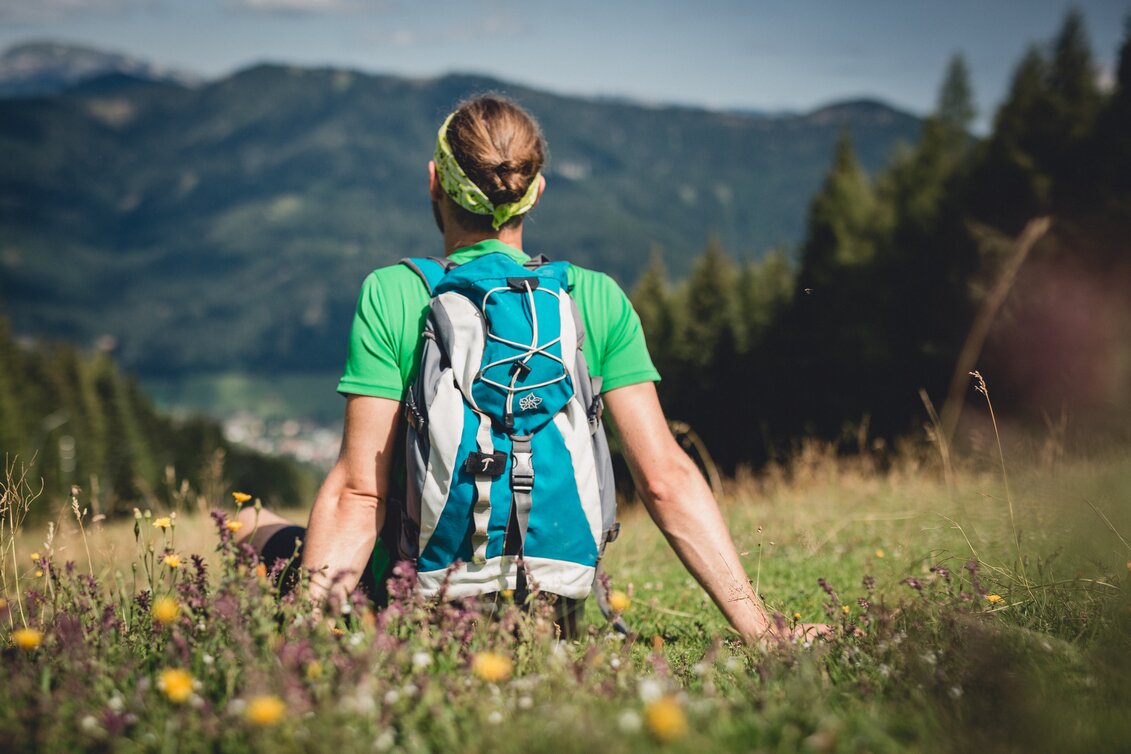 Ein Wanderer sitzt auf einer Wiese und blickt in die Ferne