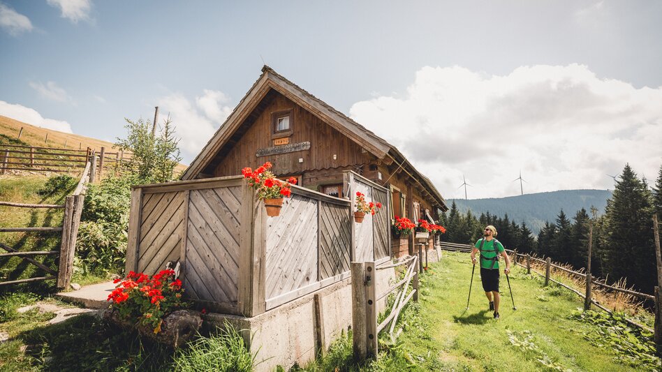 Eine Almhütte und ein Wanderer der um die Ecke kommt