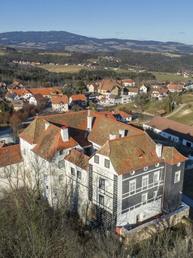 Ein großes, unvollendetes Gebäude mit roten Dächern in einer ländlichen Umgebung. Im Hintergrund sind sanfte Hügel und weitere Wohnhäuser zu sehen. | © Schlösserstraße