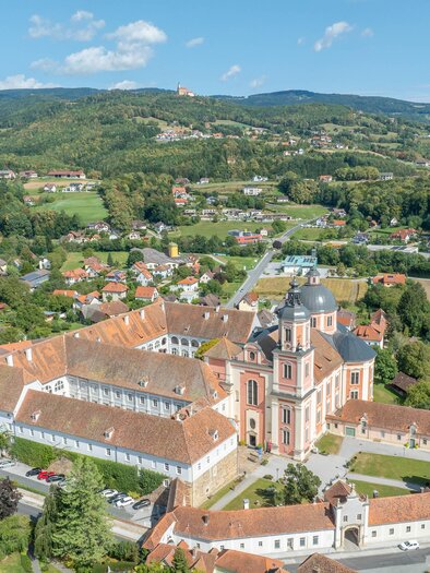A picturesque view of a monastery with beautiful buildings and a landscape in the background. The surroundings consist of forests and small villages. | © Helmut Schweighofer